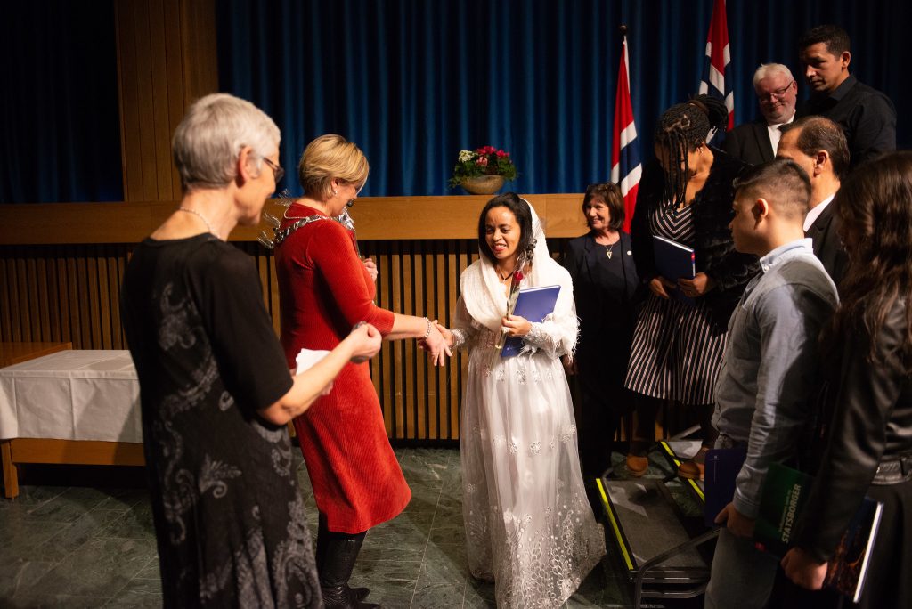 Bilde av statsborgerseremoni i Steinkjer. Her får en dame i hvit kjole sitt statsborgerskap.